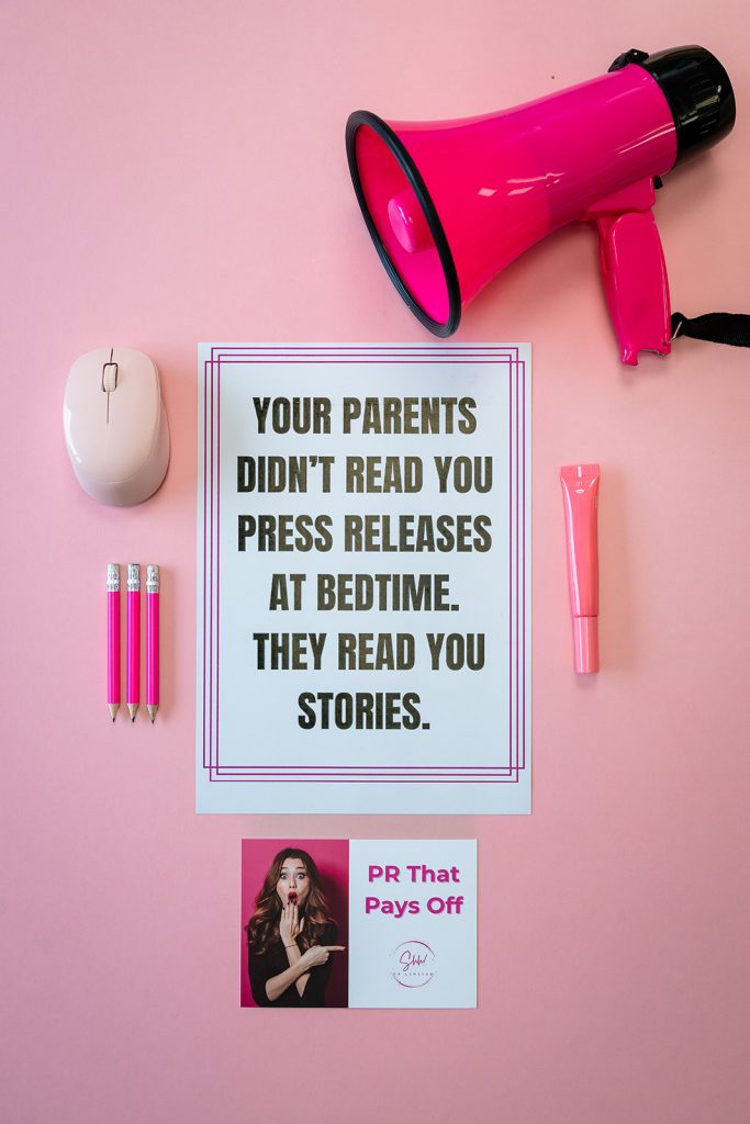 Image shows a flat lay set up on a pale pink background. On the pink background is a sign that reads "your parents didn't ready you press releases at bedtime, they read you stories." The sign is surrounded by pink pencils, a pink mouse, a pink lipgloss, a pink megaphone and a postcode that reads "PR that pays off."